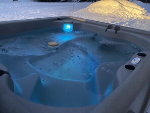 Un bain à remous avec un éclairage bleu, entouré de neige.