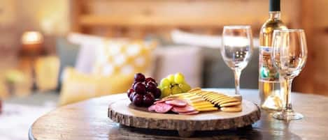 Uma mesa de madeira com uma tábua de frios, uvas e taças de vinho.