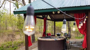 Un jacuzzi bajo una zona techada con cortinas rojas y luces colgantes.