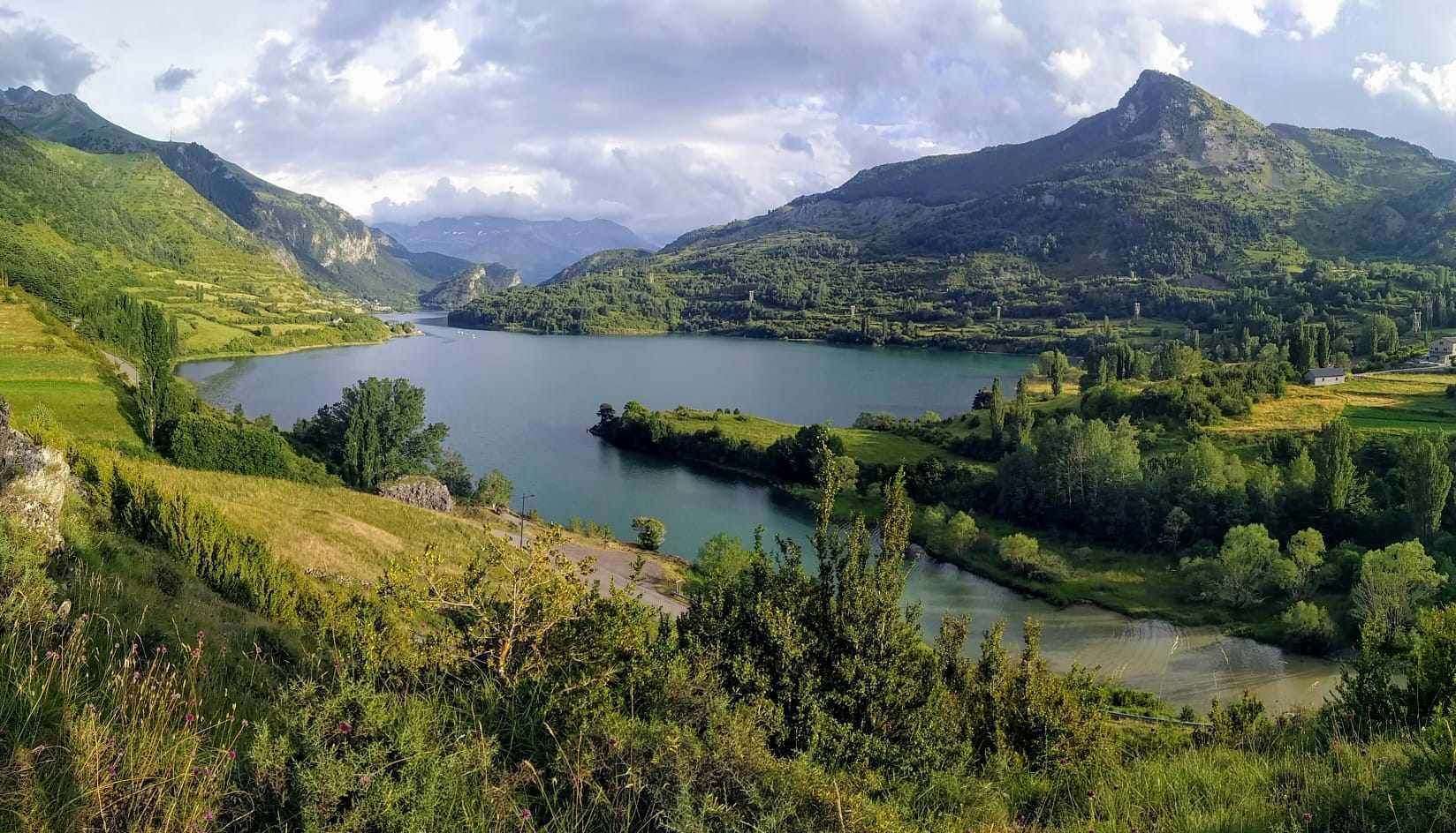 A mountainous landscape with a lake, green fields, and a few buildings in the distance.
