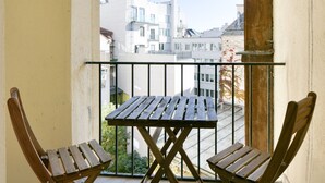 A balcony with a wooden table and two chairs, overlooking a cityscape with modern buildings.