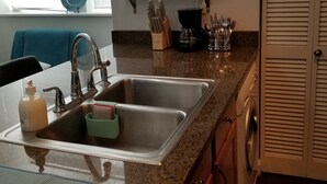 Una cocina con un lavamanos de acero inoxidable, una cafetera y una planta en un estante.
