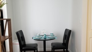 Un comedor con una mesa redonda, dos sillas, un armario blanco pequeño y una estantería.