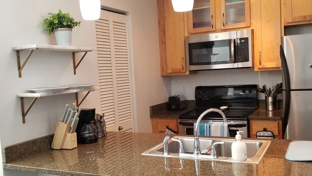 Una cocina moderna con encimeras de granito, electrodomésticos de acero inoxidable, armarios de madera e iluminación colgante.