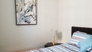 Un dormitorio con cama, mesita de noche, lámpara y un cuadro abstracto colgado en la pared.
