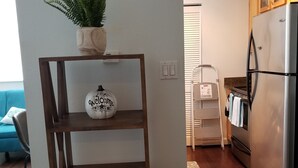 Una cocina con un estante de madera que sostiene una planta, un cartel de bienvenida y un libro de ajedrez.