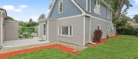 A two-story house with a sloped roof, a covered patio, and a well-maintained lawn.