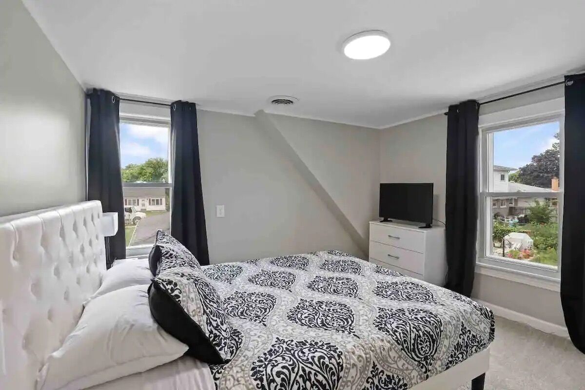 A bedroom with a bed, a TV, and a window with curtains.