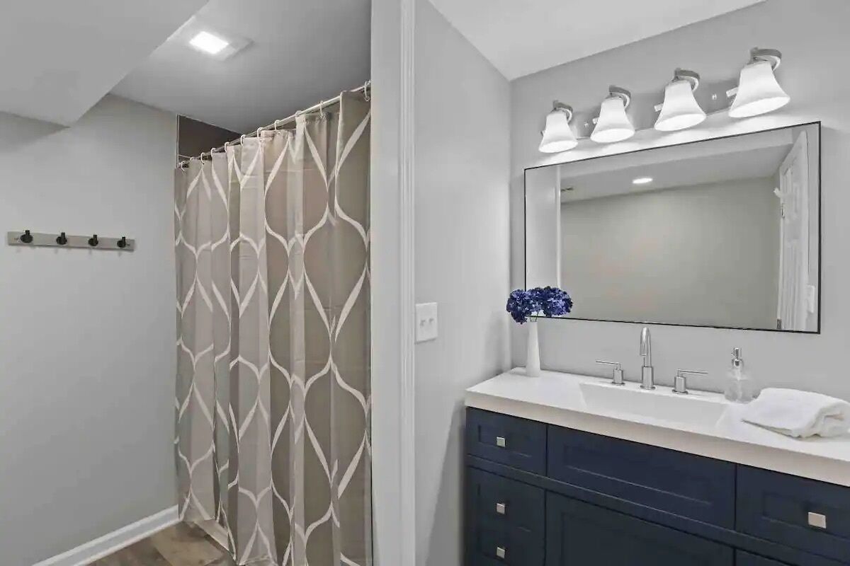 Un baño moderno con cortina de ducha, un espejo grande y un tocador con lavamanos y armarios.