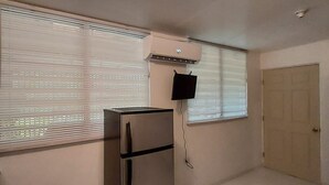 A room with a stainless steel refrigerator, an air conditioning unit, a mounted television, and a door.