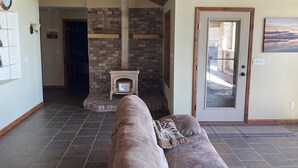 A cozy living room with a stone fireplace, a wooden ceiling, and a door leading outside.