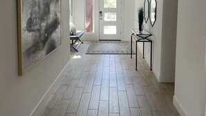 A hallway with a wooden floor, a large abstract painting, a door with a glass panel, and a small table with a plant. - Arizona retreat! Hiking trails, 15 mins. to Downtown. Heated community pool. (Phoenix)