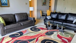 Ein Wohnzimmer mit zwei schwarzen Ledersofas, einem Couchtisch und einem bunten Teppich.