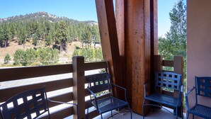 A balcony with wooden railings and metal chairs, overlooking a forested hillside. - Village at Palisades Tahoe Condo #6, in Building 5, Ski In/Out, with Mountain View!! (Olympic Valley)