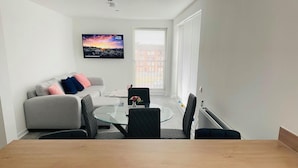 Ein modernes Wohnzimmer mit einem grauen Sofa, einem Glastisch und einem an der Wand befestigten Fernseher.