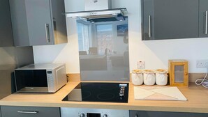 Eine moderne Küche mit integriertem Mikrowellenherd, einem Herd und einer Beko-Dunstabzugshaube. Auf der Arbeitsfläche befinden sich drei Gläser mit Kaffee, Tee und Zucker.