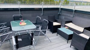 Eine Dachterrasse mit Glastisch, Korbstühlen und einer Couch.