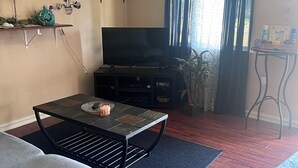 Uma sala de estar com televisão de tela plana em um suporte, um sofá cinza, uma mesa de centro e um tapete estampado.