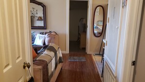 Um corredor com piso de madeira que leva a um quarto com cama, cômoda e espelho.