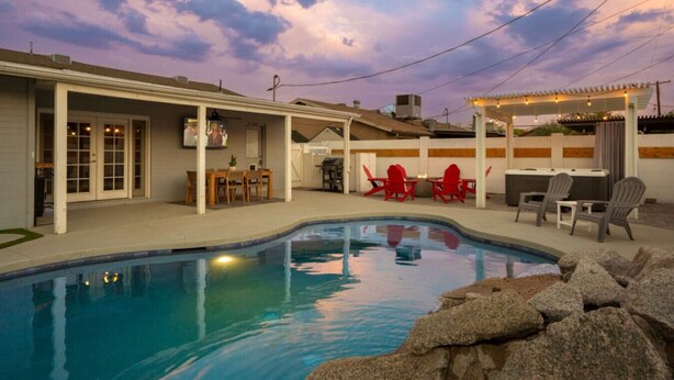 A backyard with a swimming pool, outdoor seating, and a covered patio area.