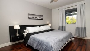 A modern bedroom with a large bed, a nightstand, a ceiling fan, and a window with curtains.