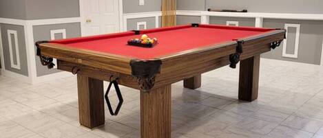 A pool table with a red felt surface, surrounded by a light-colored tiled floor.