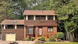 A two-story house with a garage, a front porch, and a well-maintained lawn. - Whispering Pines Riverside Getaway (Kawartha)