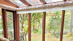 A sunroom with large windows, two patterned armchairs, and a view of a wooded area. - Whispering Pines Riverside Getaway (Kawartha)