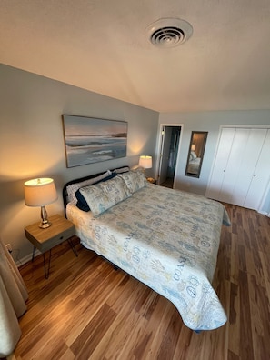 Ein Schlafzimmer mit Bett, Nachttisch, Lampe, einem Bild an der Wand und einem Kleiderschrank.