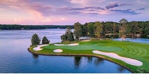 Un parcours de golf bordé d’eau sur trois côtés, entouré d’arbres et offrant une vue sur un ciel dégagé.