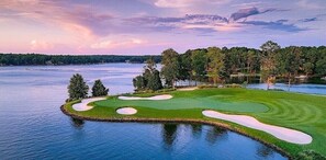 A golf course with water on three sides, surrounded by trees and a clear sky.