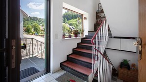 A staircase with a red handrail leading to a landing with a window overlooking a green landscape. - Cozy vacation apartment in spa town in the southern Black Forest with mountain view, garden & Wi-Fi (Todtmoos)
