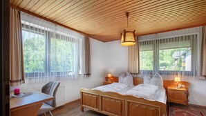 A bedroom with a wooden bed, two bedside tables with lamps, a desk, and a chair. - Cozy vacation apartment in spa town in the southern Black Forest with mountain view, garden & Wi-Fi (Todtmoos)