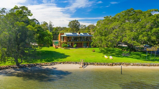 Una casa de dos plantas con un amplio jardín delantero y una zona de playa arenosa.