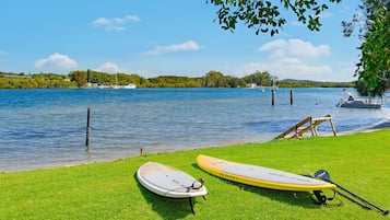 A grassy lakeside area with paddleboards and a boat.