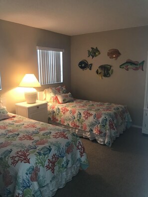 A bedroom with two beds, a nightstand, a lamp, a window with blinds, and wall decorations of fish. - Beach Front Condo, Venice, Florida. 2 bedroom, 2 bath, heated pool.  (Venice)