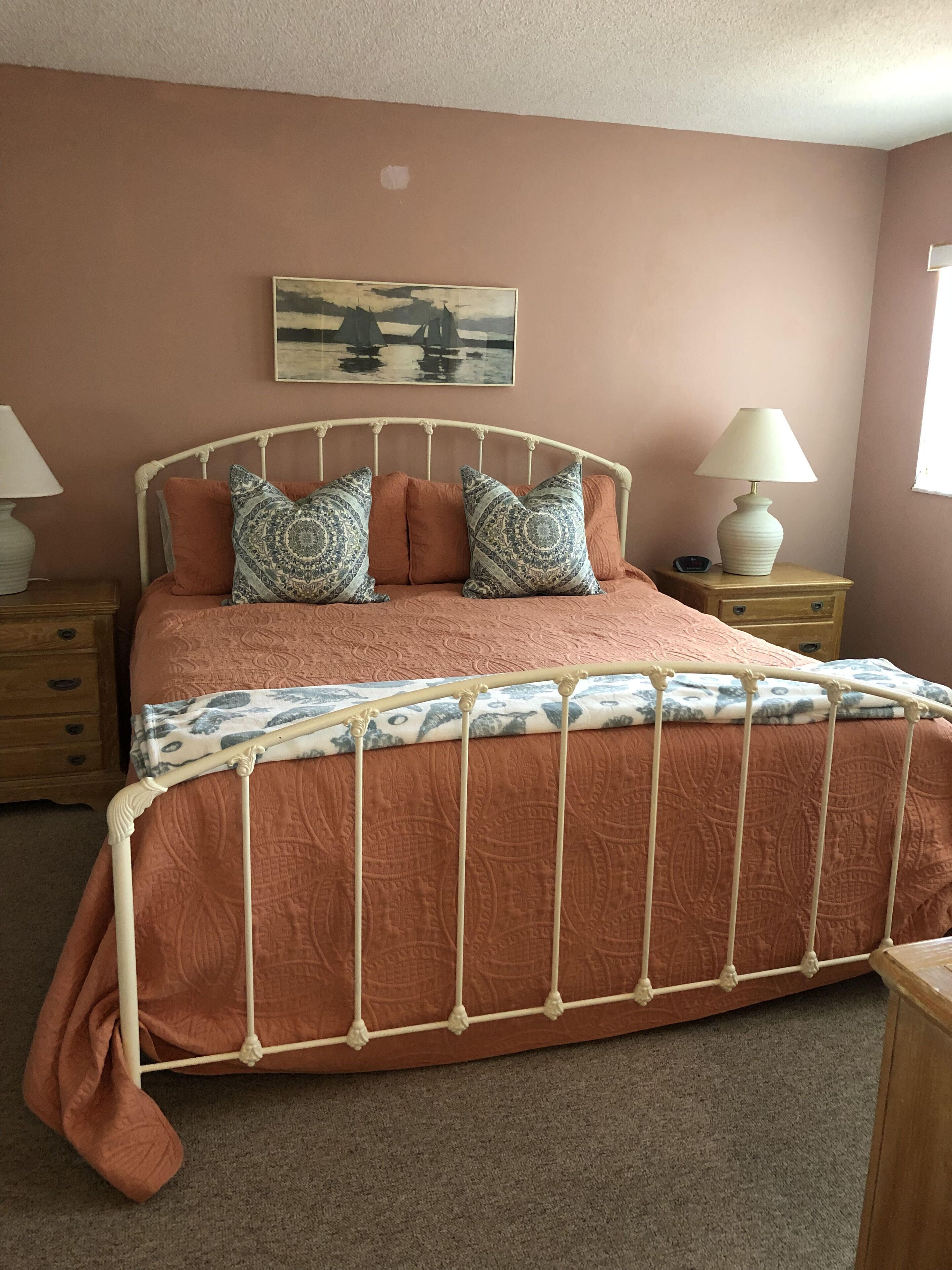 Een slaapkamer met een bed met metalen frame, een beddengoed met patroon en twee nachtkastjes met lampen.