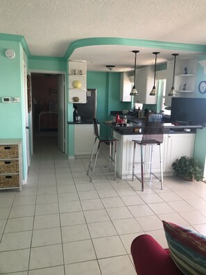A kitchen with a dining area, a refrigerator, a sink, and a stove. There is a chair and a table in the dining area. - Beach Front Condo, Venice, Florida. 2 bedroom, 2 bath, heated pool.  (Venice)