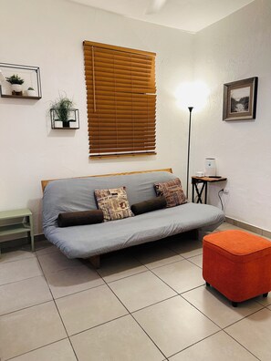 Una sala de estar con un sofá, una mesita, una lámpara de pie y un reposapiés rojo.