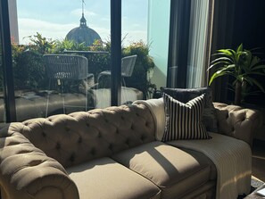 A beige tufted sofa with striped pillows, a glass table, and chairs, with a view of a dome-shaped building through large windows. - Degraves Studio Apartment-hotel luxury with the comfort of home in Melbourne CBD (Melbourne)