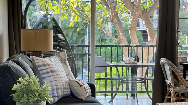 Un salon avec un canapé bleu foncé, une petite table ronde ornée d’une plante, et une vue sur un balcon aménagé avec du mobilier d’extérieur.