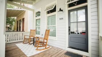 A porch with wooden rocking chairs, a white railing, and a door marked with the number 906.