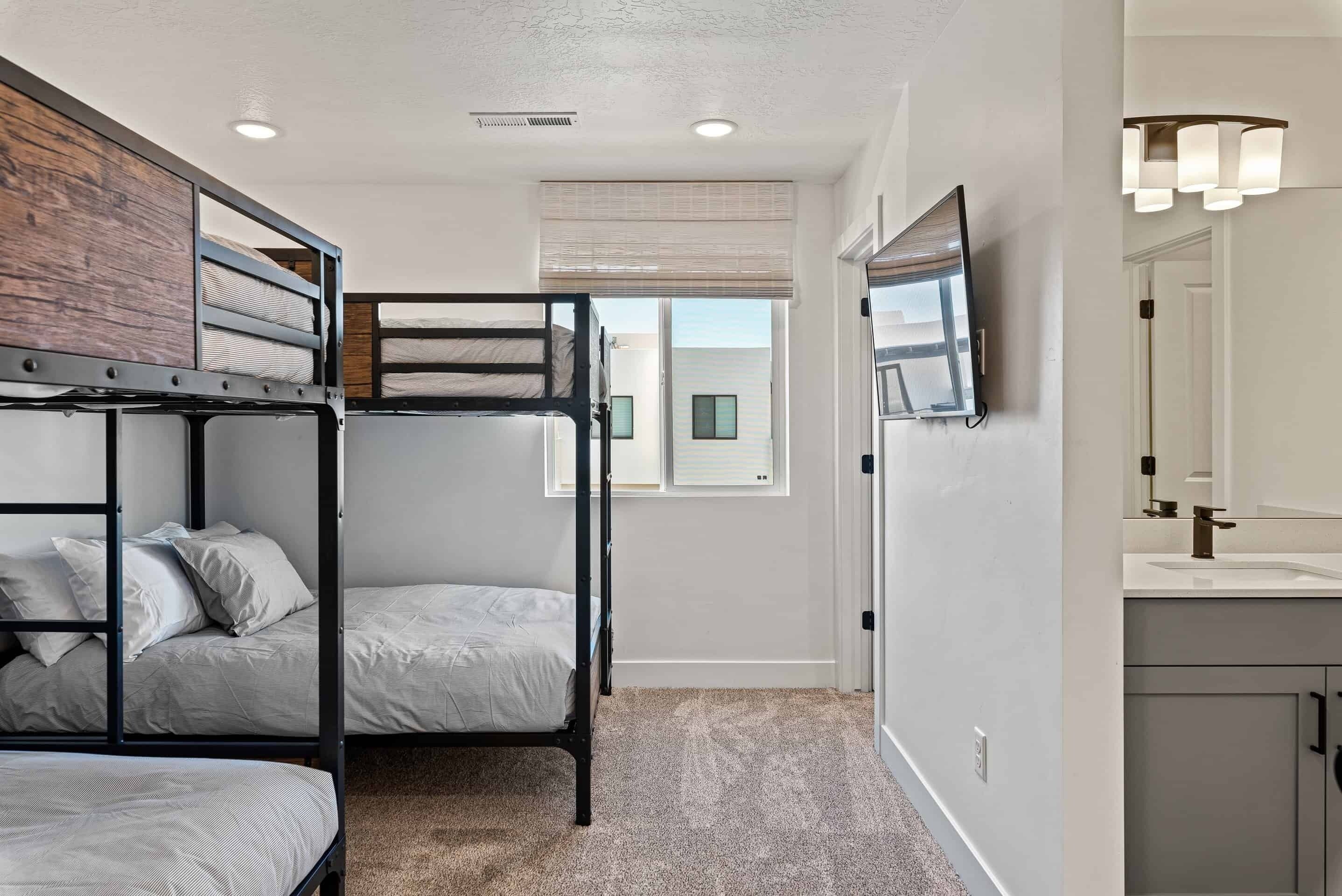 A room with bunk beds, a TV mounted on the wall, and a bathroom with a mirror and sink.