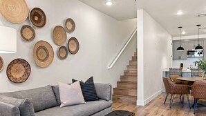 A modern living room with a grey sofa, a black bench, and a staircase leading to a kitchen area. - Serenity Shores #80 (St. George)