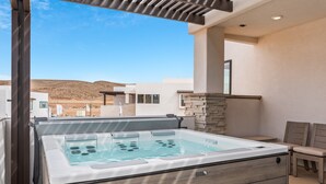 A hot tub with a wooden base, a stone wall, and a view of a desert landscape. - The Berber at Desert Color by RedAwning (St. George)