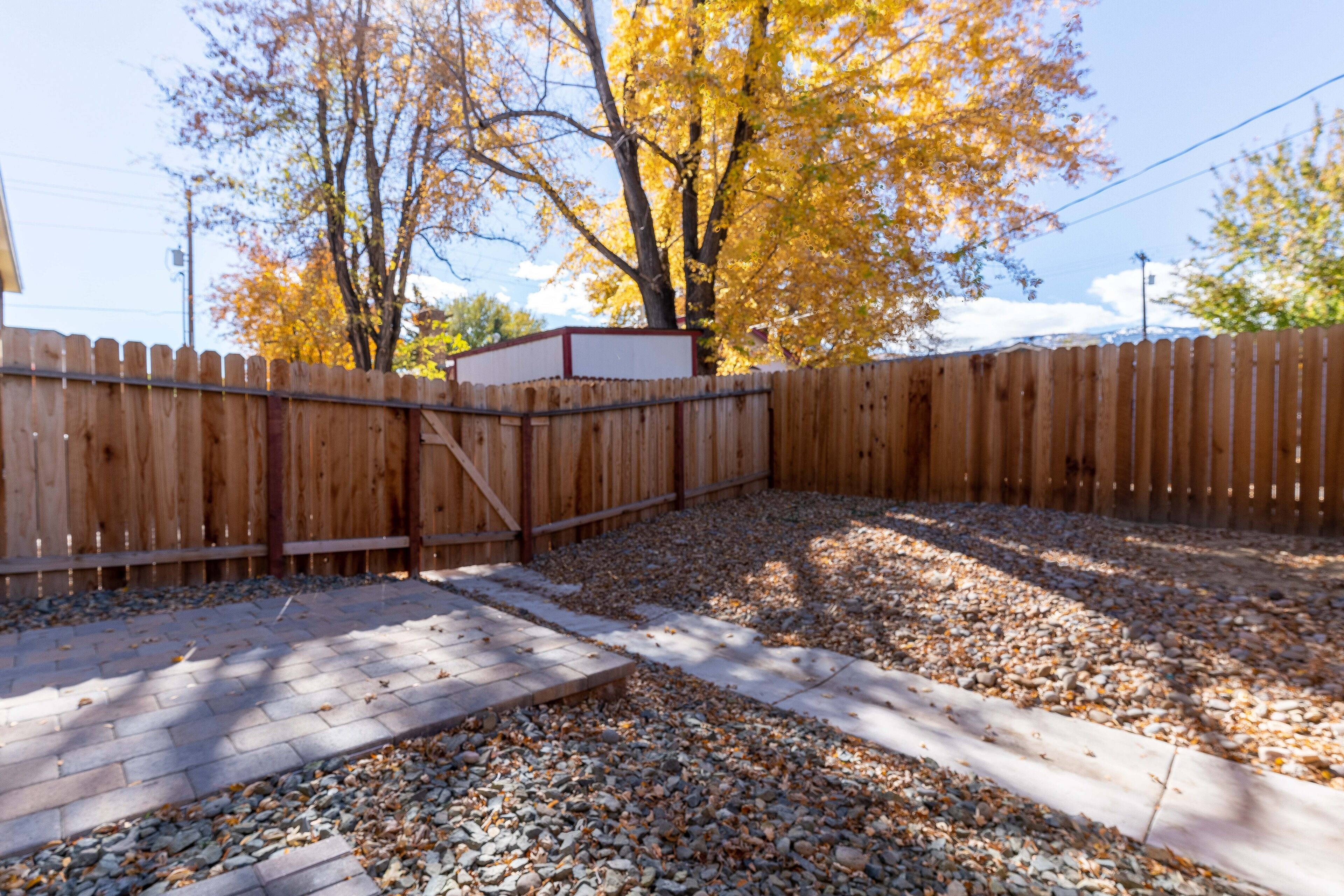 A backyard with a wooden fence, gravel, and a paved area.