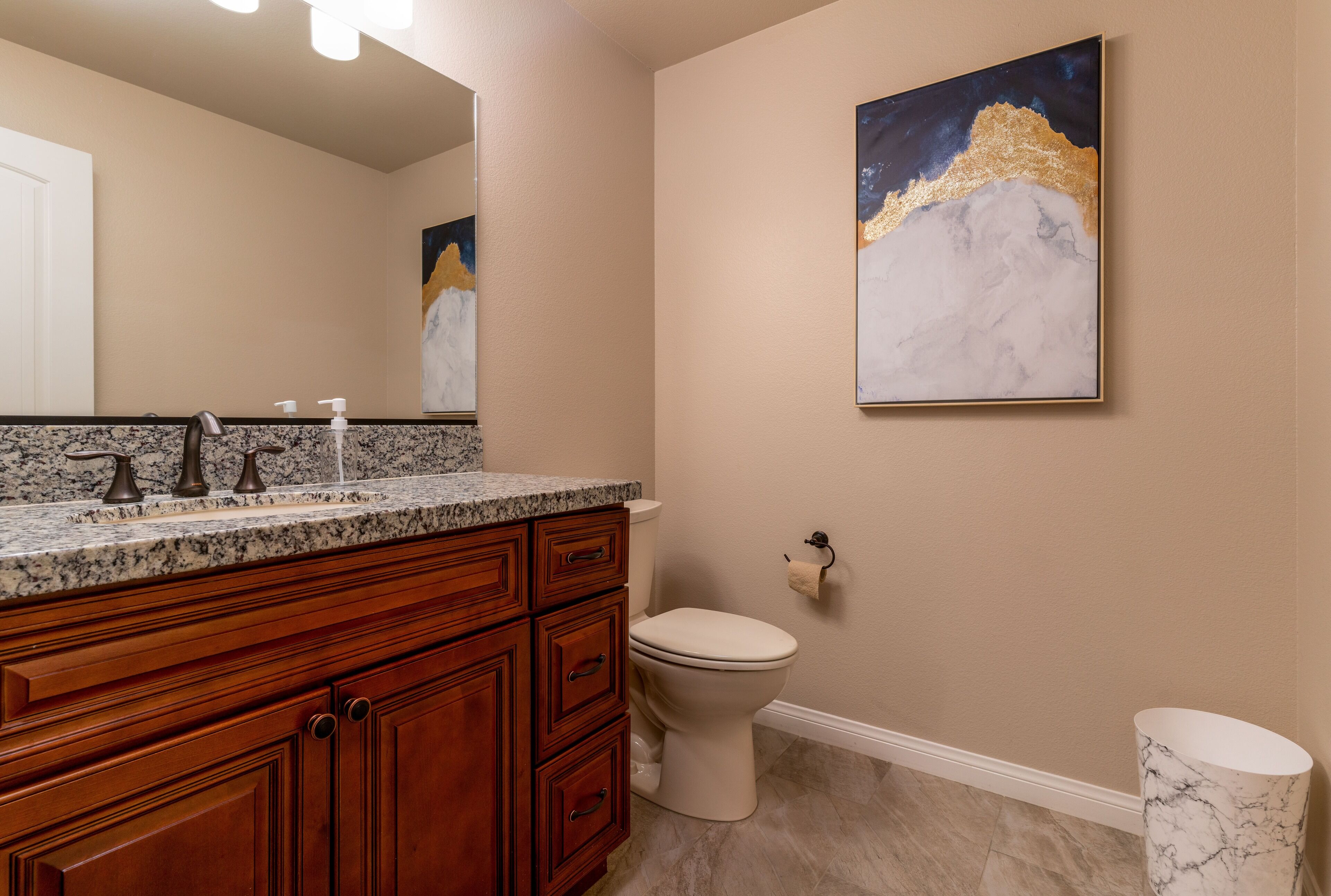 A bathroom with a marble countertop, wooden cabinets, a toilet, and a marble floor.