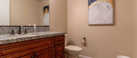 A bathroom with a marble countertop, wooden cabinets, a toilet, and a marble floor.
