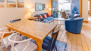 Amplia sala de estar con una mesa de comedor de madera, sofás azules y un gran ventanal que da a un patio exterior.