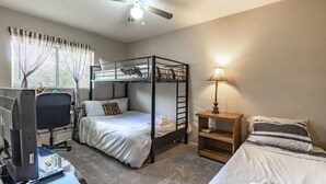 Une chambre avec un lit superposé, un bureau avec un ordinateur, une lampe et une fenêtre avec des rideaux.
